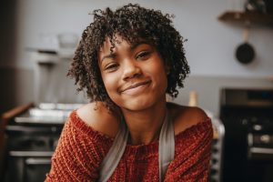Close-up portrait of smiling female student with curly hair standing against wall in cooking class