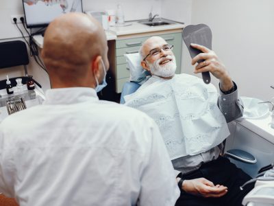 Old man sitting in the dentist’s office Handsome old man talking to the dendist. Two men in the dentist's office. Grandfather looking into the mirror on his teeth